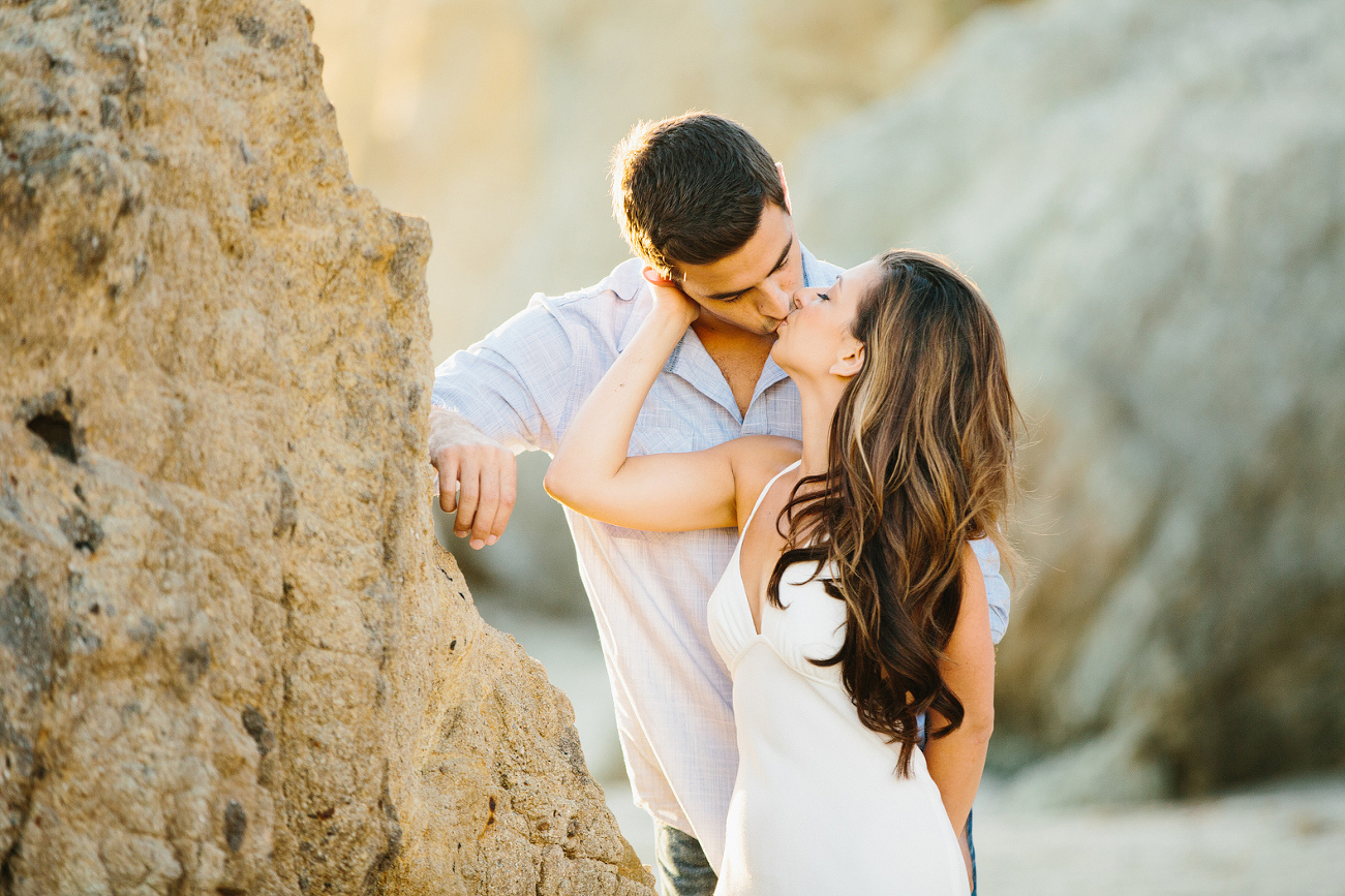 The couple kissing by a rock. 