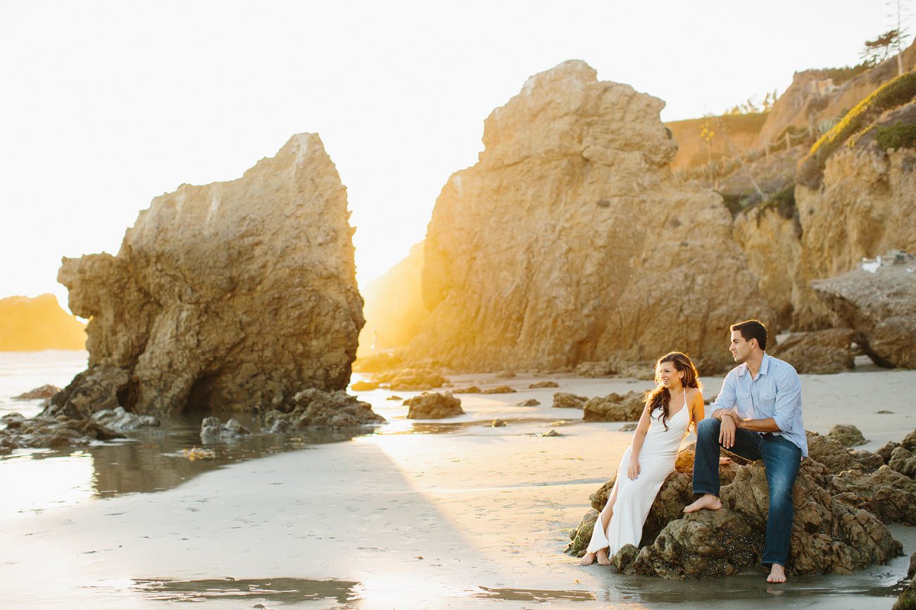 The couple sitting on rocks at the beach. 