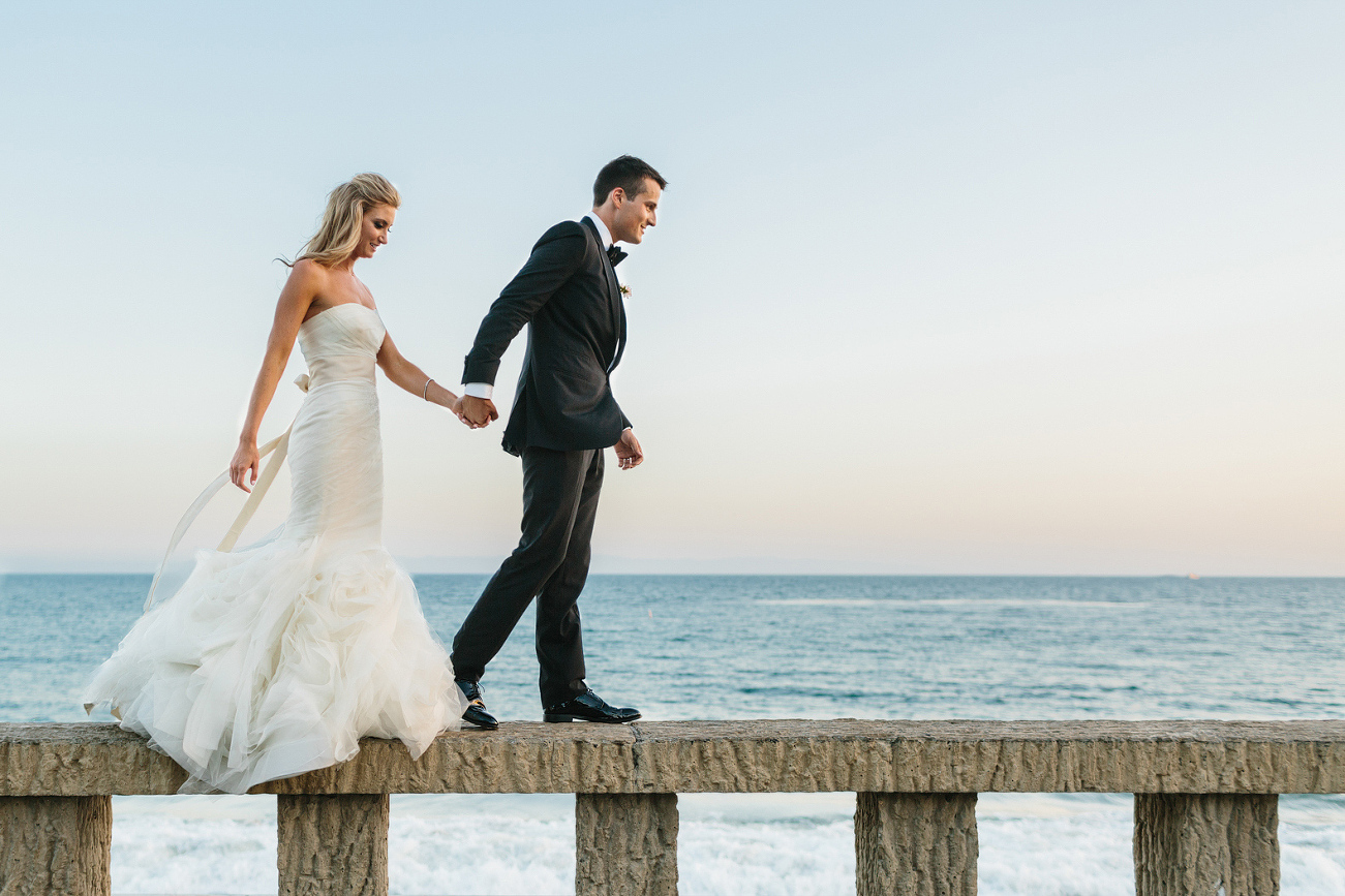 Jaclyn and Nick walking on a wall at the beach. 