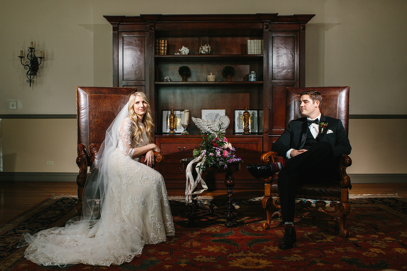 The bride and groom sitting in two leather chairs. 