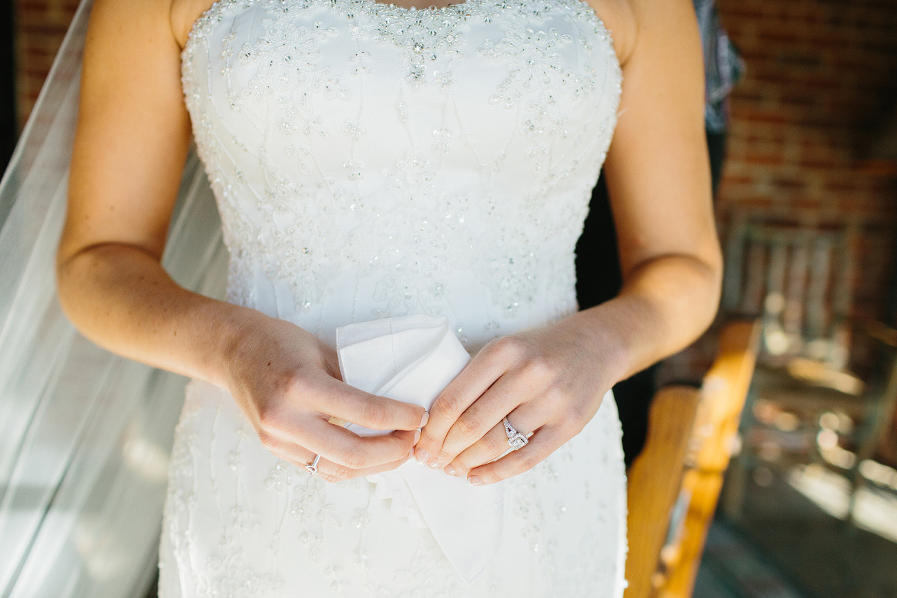 The bride holding a hanky in front of her beaded wedding dress. 