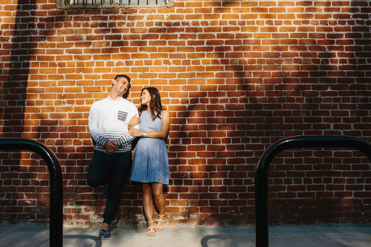 The engaged couple in front of a brick wall. 