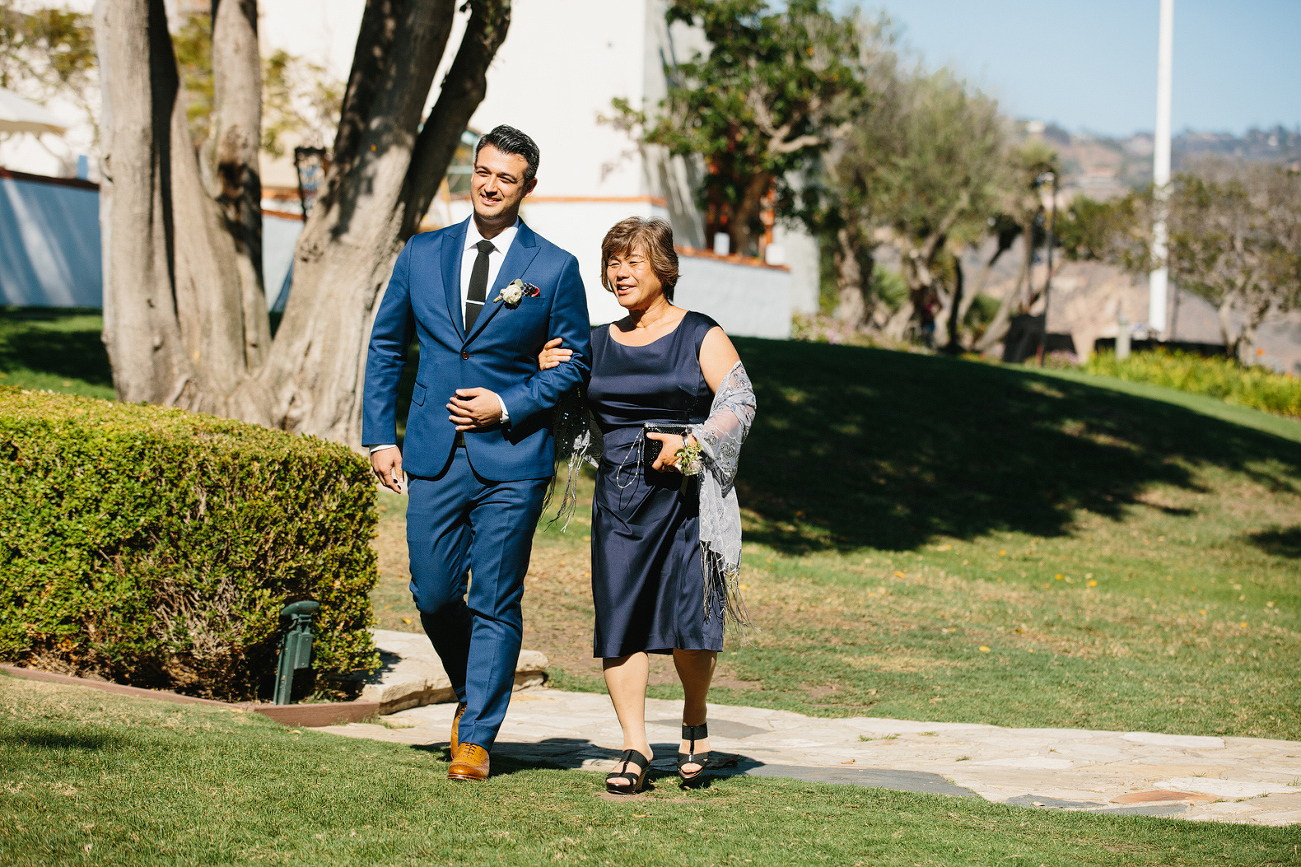 The groom walking down the aisle with his mother. 