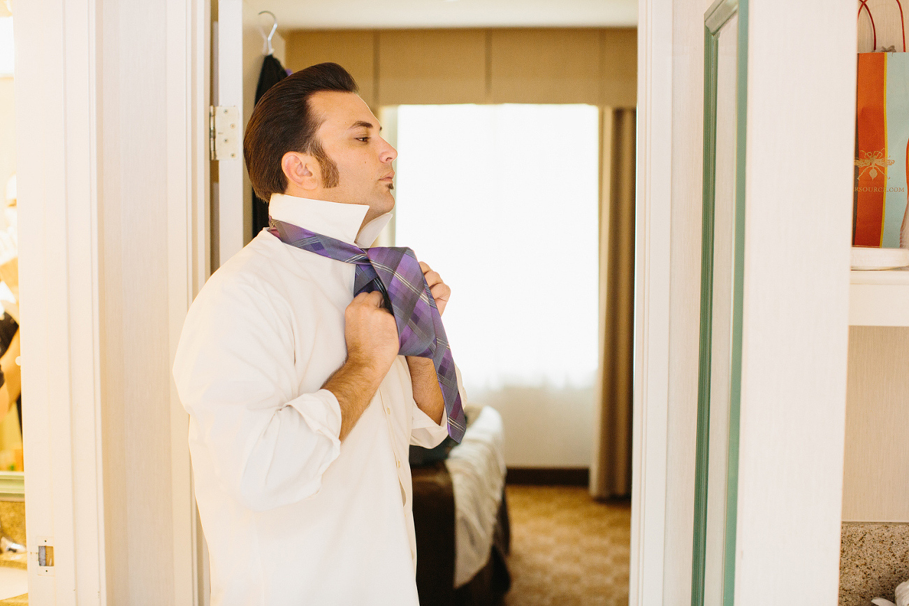 The groom tying his purple tie. 