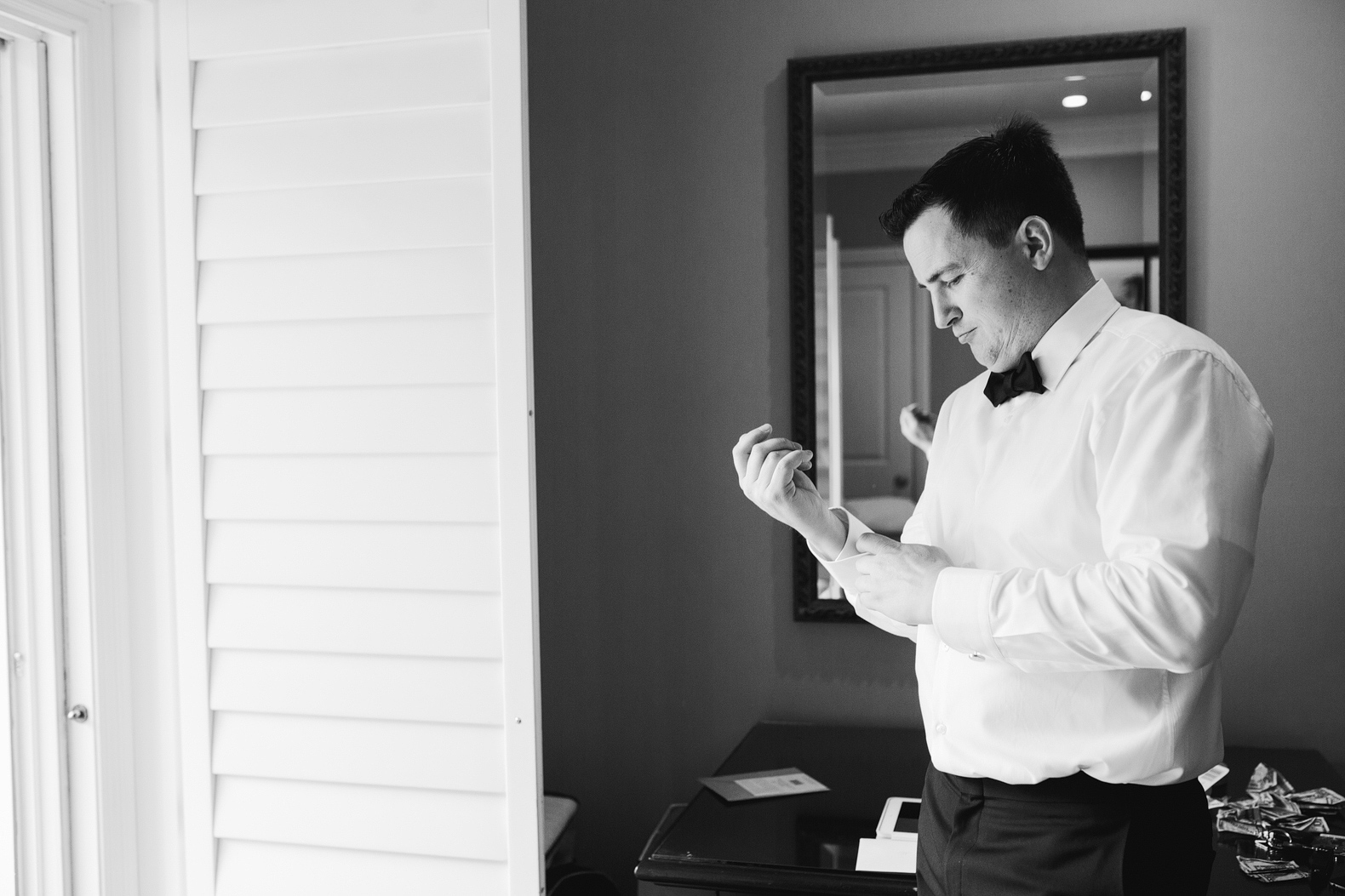 A black and white portrait of the groom getting dressed. 