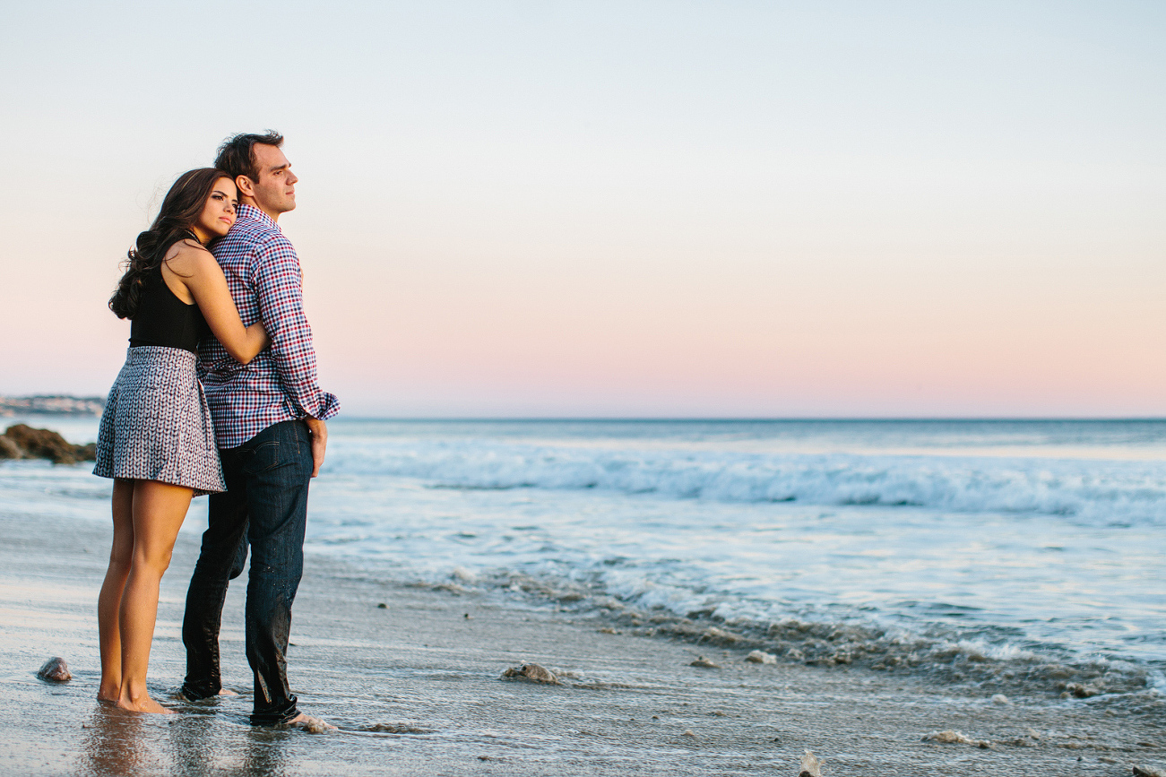 The couple standing on the beach at sunset. 