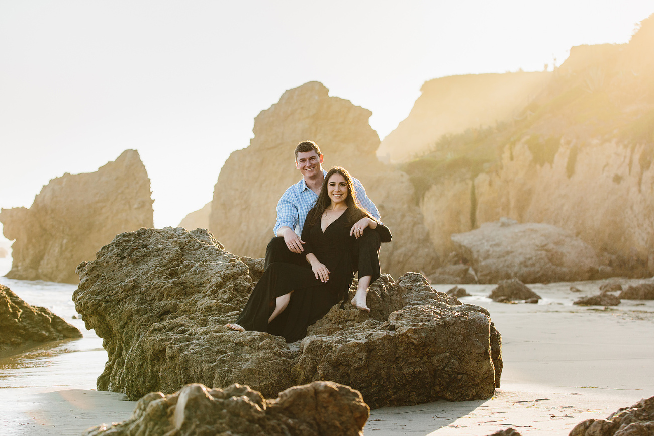 fiances at the beach sitting together smiling looking at the camera