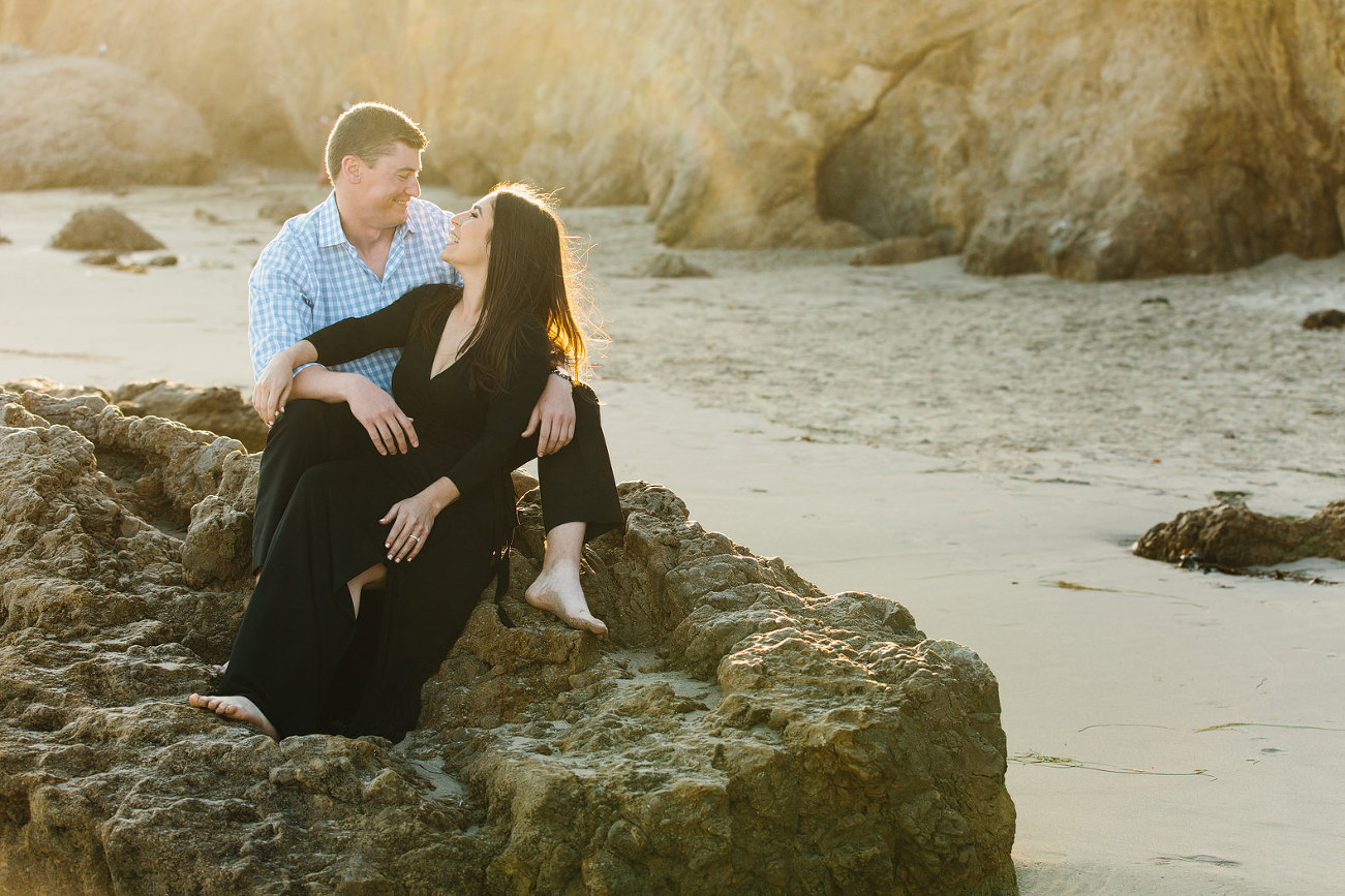 Couple sitting on rock at the beach in warm glow of the sun