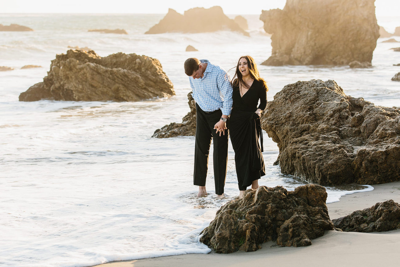 fun photo at engagement session of the couple feeling the water hit their feet.