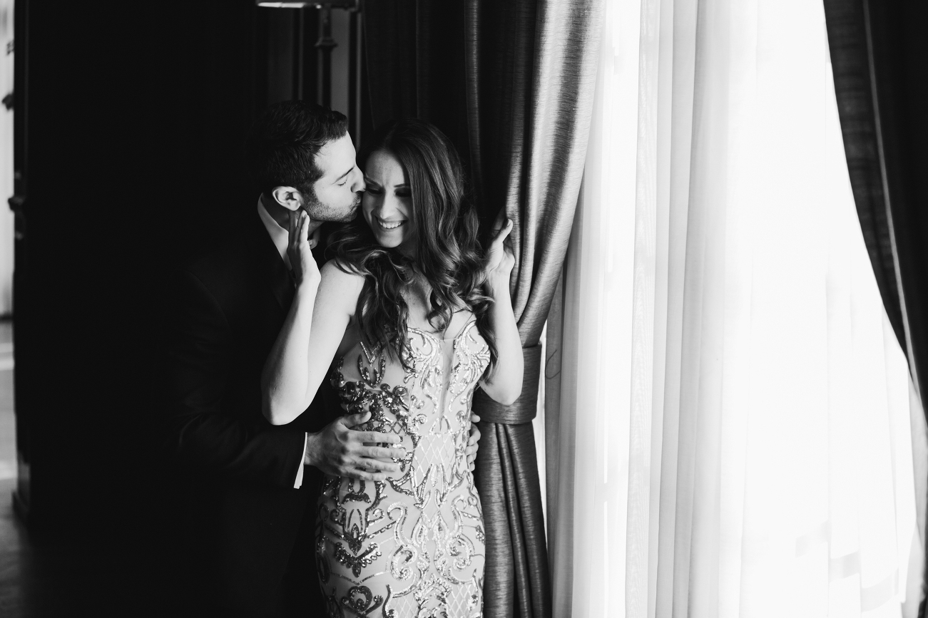 bride and her fiance share a kiss at a window